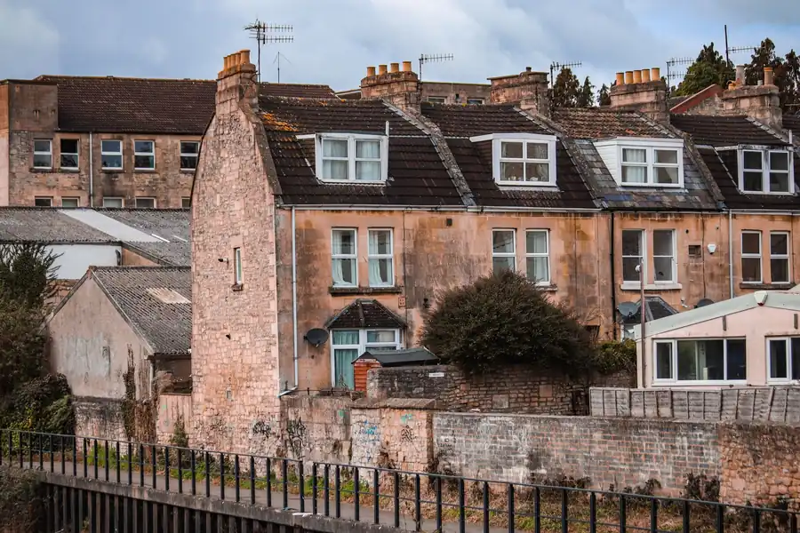 Row of stone townhouses with chimneys and dormer windows behind a brick wall by the water