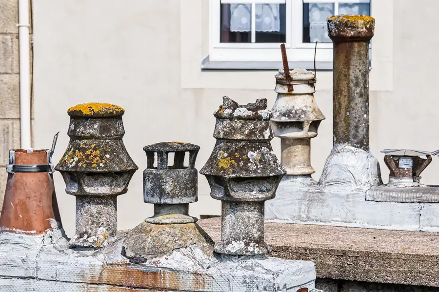 Weathered chimney pots arranged on a stone ledge beside a window and wall