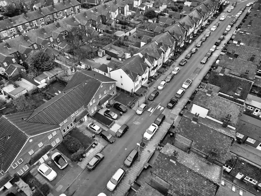 Aerial view of a residential street lined with parked cars and houses.