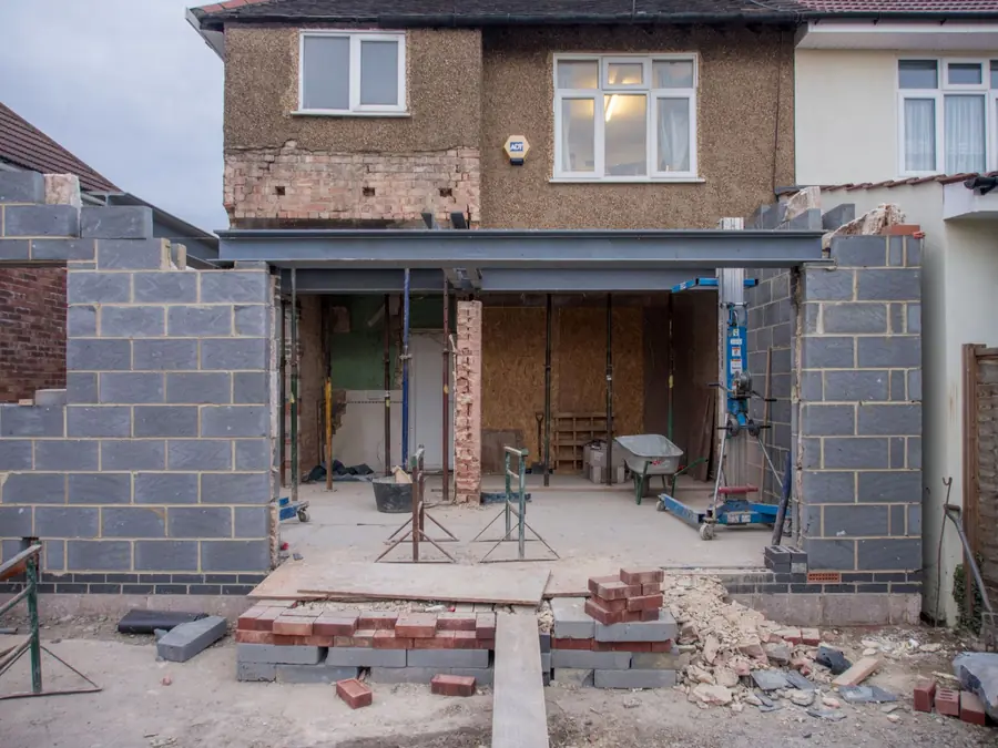 House under renovation with a large open front extension and construction debris in the driveway