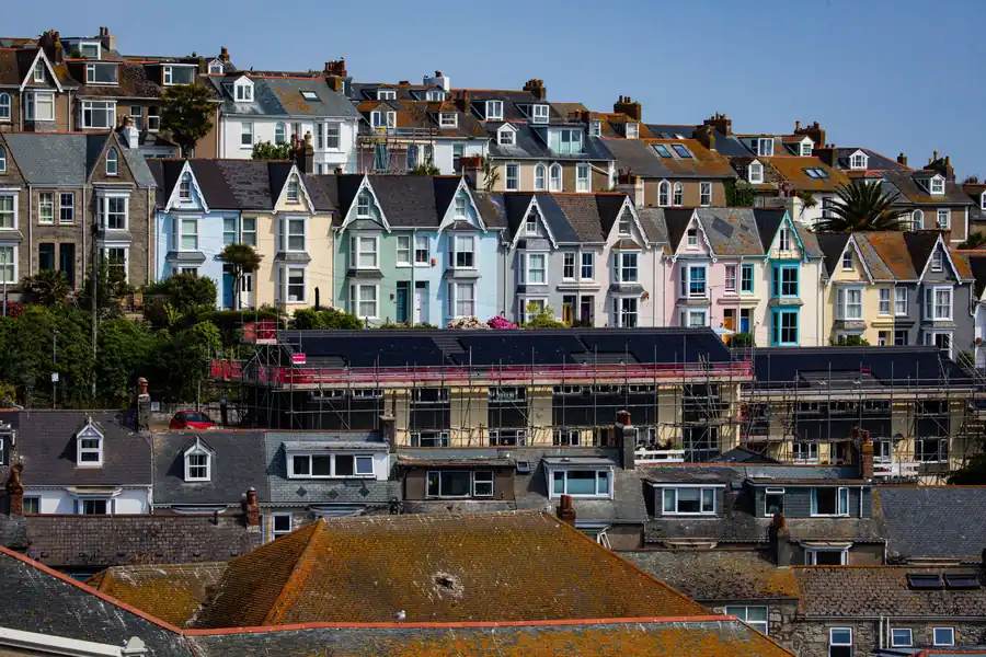 Row of pastel seaside houses on a hillside above a harbor under a clear blue sky
