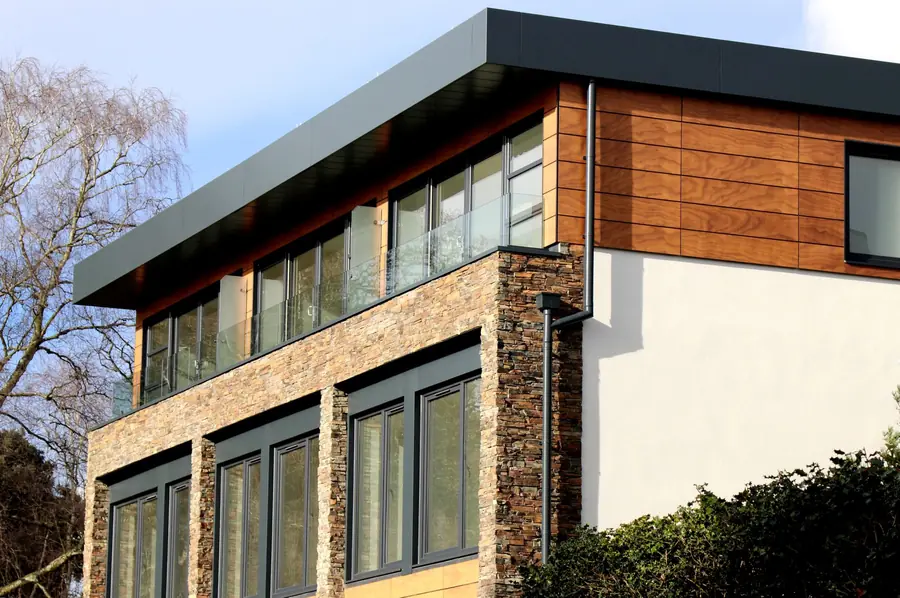 Modern building facade with large windows, stone and wood panels, and a dark roofline