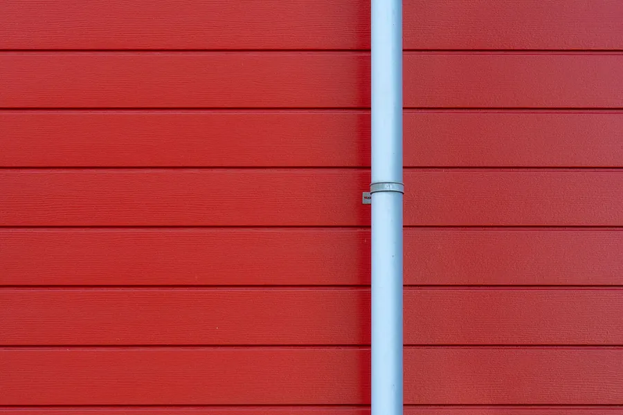 Red wooden wall with a vertical white pipe in the center
