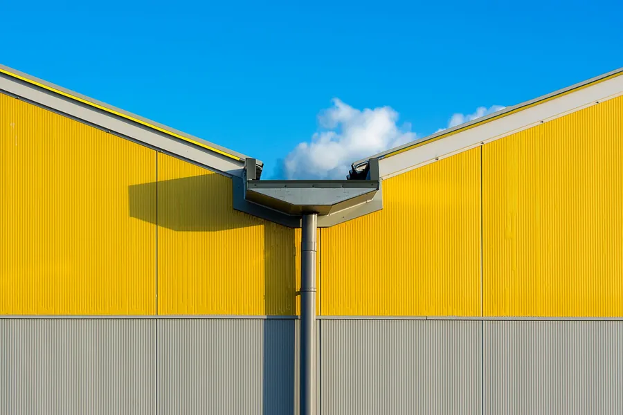 Yellow industrial building with gray lower walls and a central metal gutter against a blue sky