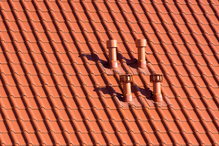 Three chimney vents on a red tiled roof, casting sharp shadows in sunlight