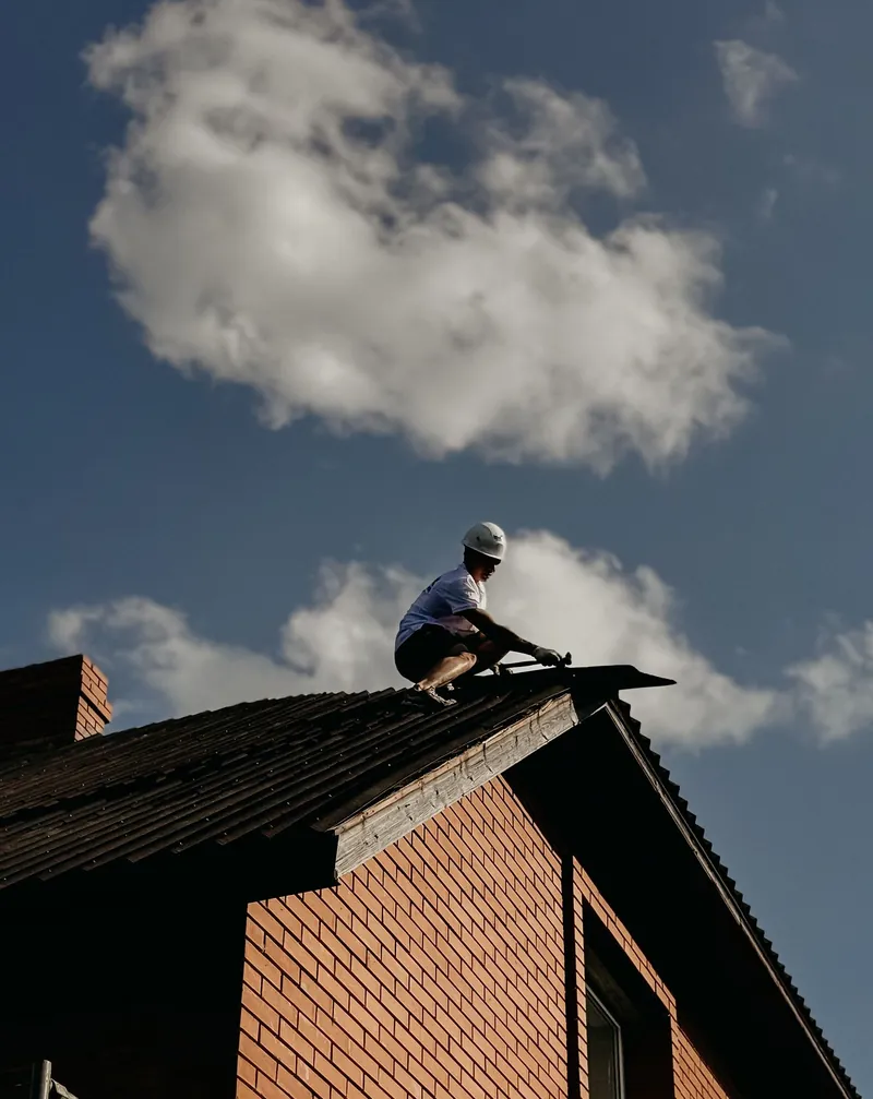 Person working on a brick roof under a cloudy sky.