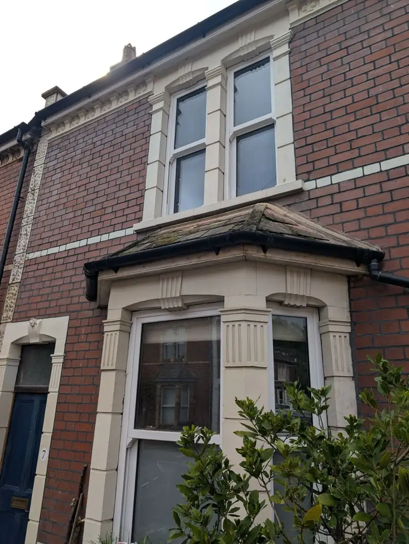 Brick row house with white bay window and small porch, viewed from the street