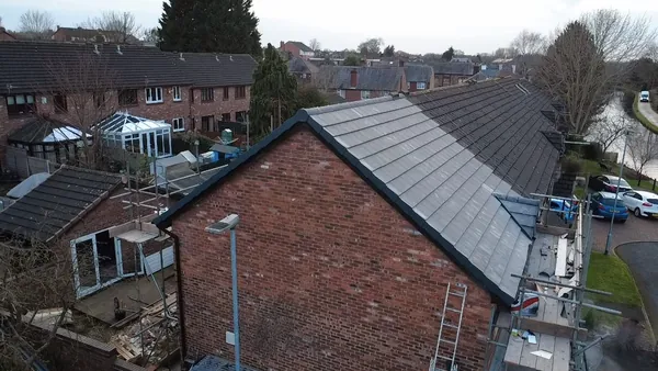 An elevated view of a brick house with a newly tiled roof, scaffolding, and surrounding homes in a residential area.
