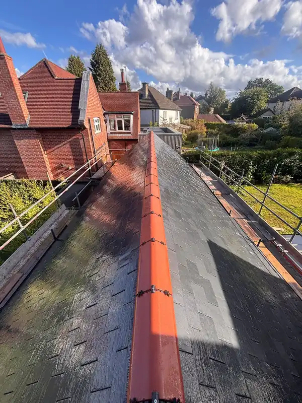 A view along a ridgeline of a dark slate roof, featuring a bright orange ridge tile and surrounding residential rooftops.