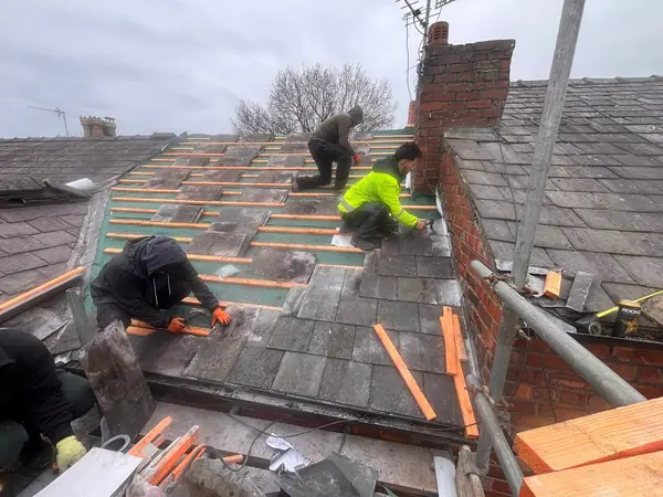 Construction workers in high-vis gear installing slate tiles on a residential roof.