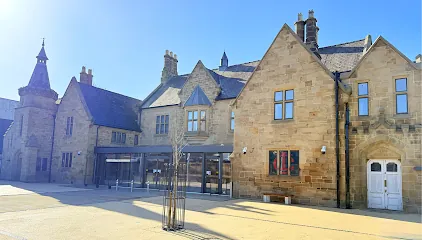 Sunny view of stone historic buildings with shopfronts and paved square