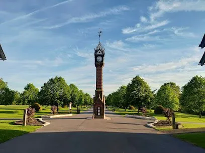 Clock tower in a landscaped park, centered on a path under a blue sky.