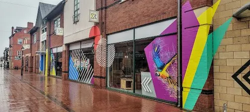Rainy street with colorful mural-covered shopfronts and reflections on the wet pavement